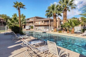 A pool area with lounge chairs and palm trees, surrounded by a multi-story building with balconies. - Senior Games Stay | Resort Amenities (St. George)