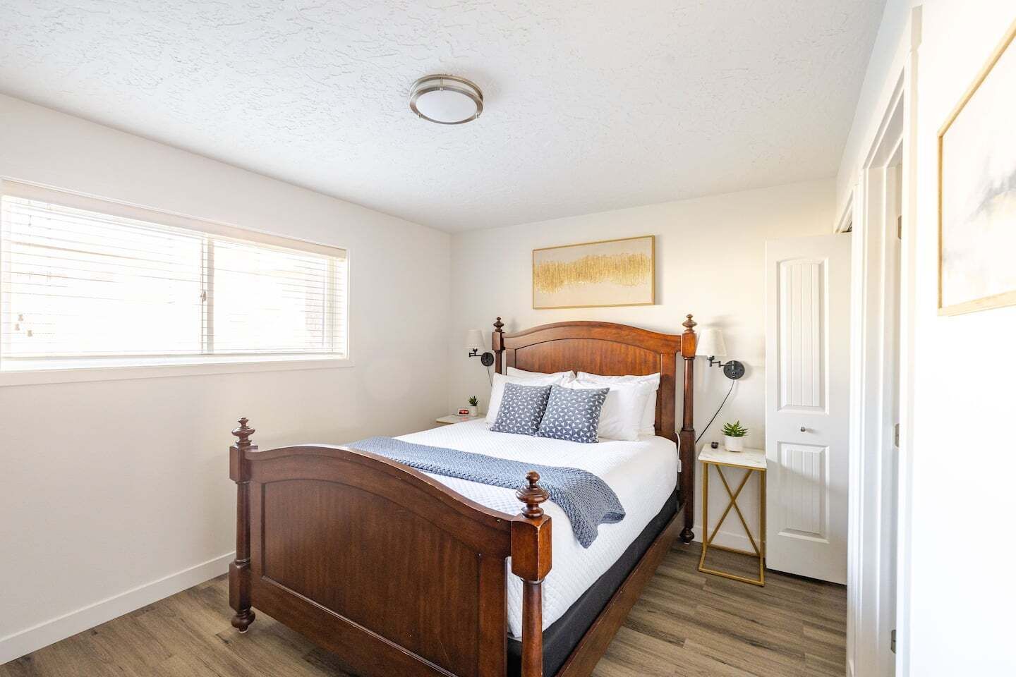 Een slaapkamer met een houten bed, nachtkastje, lamp en een raam met zonwering.
