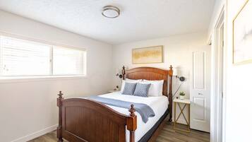 Een slaapkamer met een houten bed, nachtkastje, lamp en een raam met zonwering.