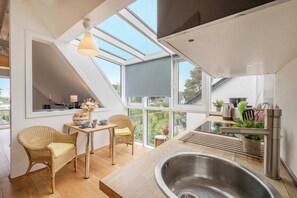 Une cuisine moderne dotée d’une verrière, un coin repas avec des chaises en osier et une grande fenêtre donnant sur un jardin.
