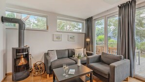 A cozy living room with a fireplace, grey sofas, a coffee table, and large windows.