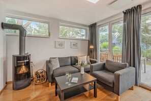 Una sala de estar acogedora con chimenea, sofás grises, una mesa de centro y ventanas amplias.