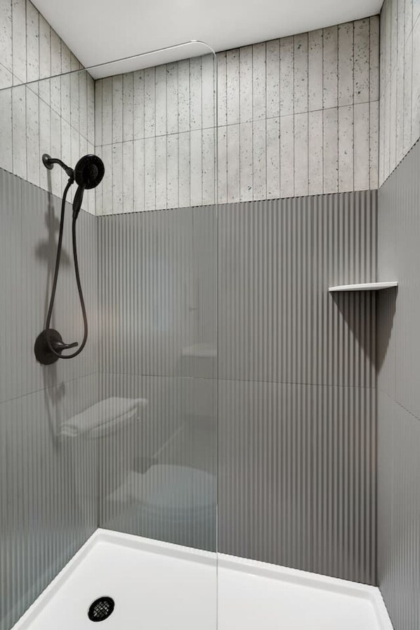 A modern shower area with a glass enclosure, a handheld showerhead, and a corner sink.