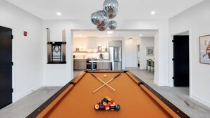 Se ve una mesa de billar con bolas, una zona de cocina y un comedor a través de una puerta abierta.
