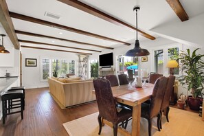 Relax in a spacious interior with a high ceiling, featuring a dining area with a wooden table and leather chairs, a comfortable seating area, and a kitchen with a countertop and sink.