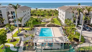 A resort with a central pool, multiple balconies, and a view of the ocean.