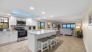 A modern kitchen with white cabinetry, a large island with stools, and a view of the ocean through the windows.