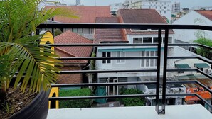 A balcony with a potted plant, a metal railing, and a view of buildings with red-tiled roofs. - Amy Hotel Hue (Hue)