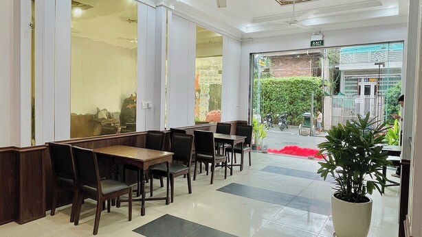 A restaurant with a modern interior, featuring a long counter with wooden tables and chairs, a ceiling with decorative elements, and a potted plant in the foreground. - Amy Hotel Hue (Hue)