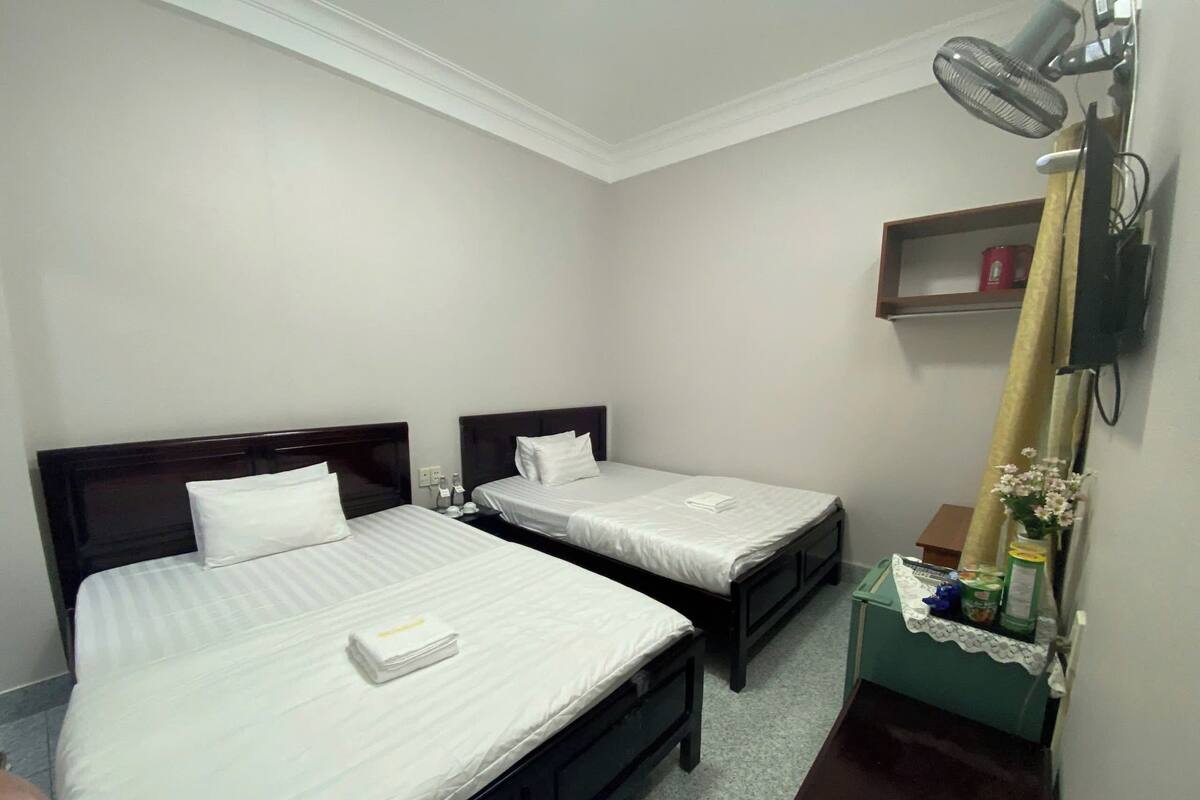 A hotel room with two single beds, a small bedside table with a lamp, a mirror, and a shelf with toiletries.