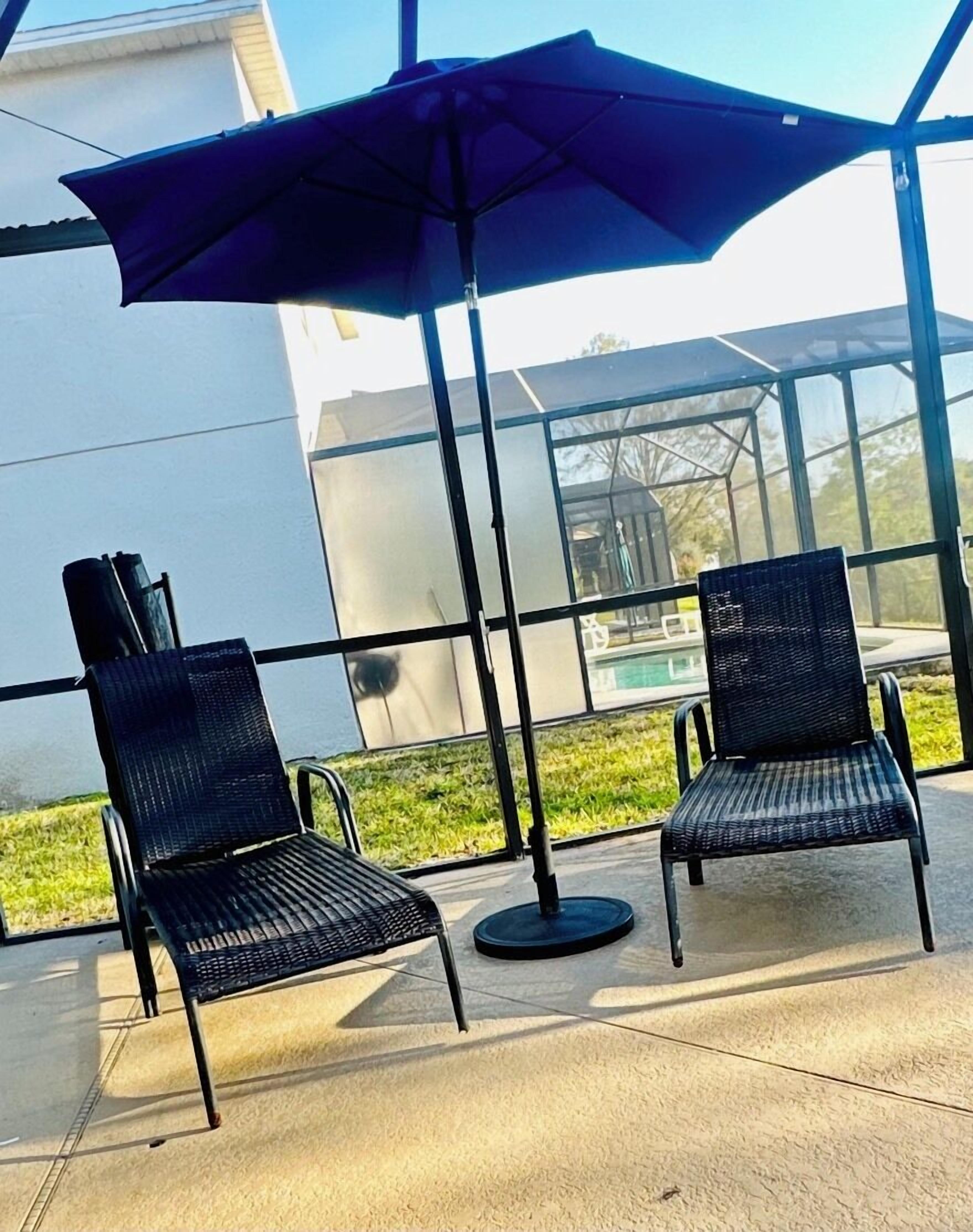 Deux chaises d’extérieur, un grand parasol, une véranda en verre et une vue sur un immeuble.