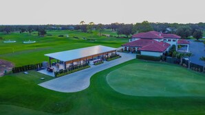 Luchtbeeld van een golfbaan met een clubhuis, een overdekt zitgedeelte en een groot huis met een rode dakbedekking.