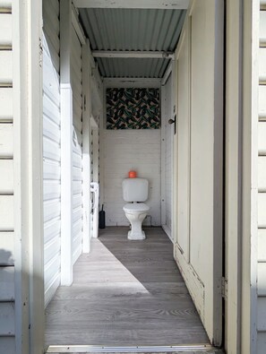 A narrow hallway leading to a toilet with a patterned wall and a wooden floor.