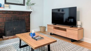 A living room with a wooden coffee table, a flat-screen TV on a wooden stand, a fireplace, and a bookshelf.