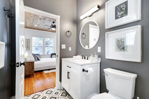 Une salle de bain avec un meuble-lavabo blanc, des toilettes, un miroir et des œuvres d’art encadrées accrochées au mur.