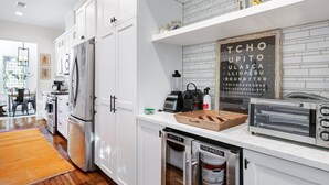 Eine moderne Küche mit weißen Schränken, einem Edelstahlkühlschrank, einem Einbauofen, einem Toaster und einer Kaffeemaschine.