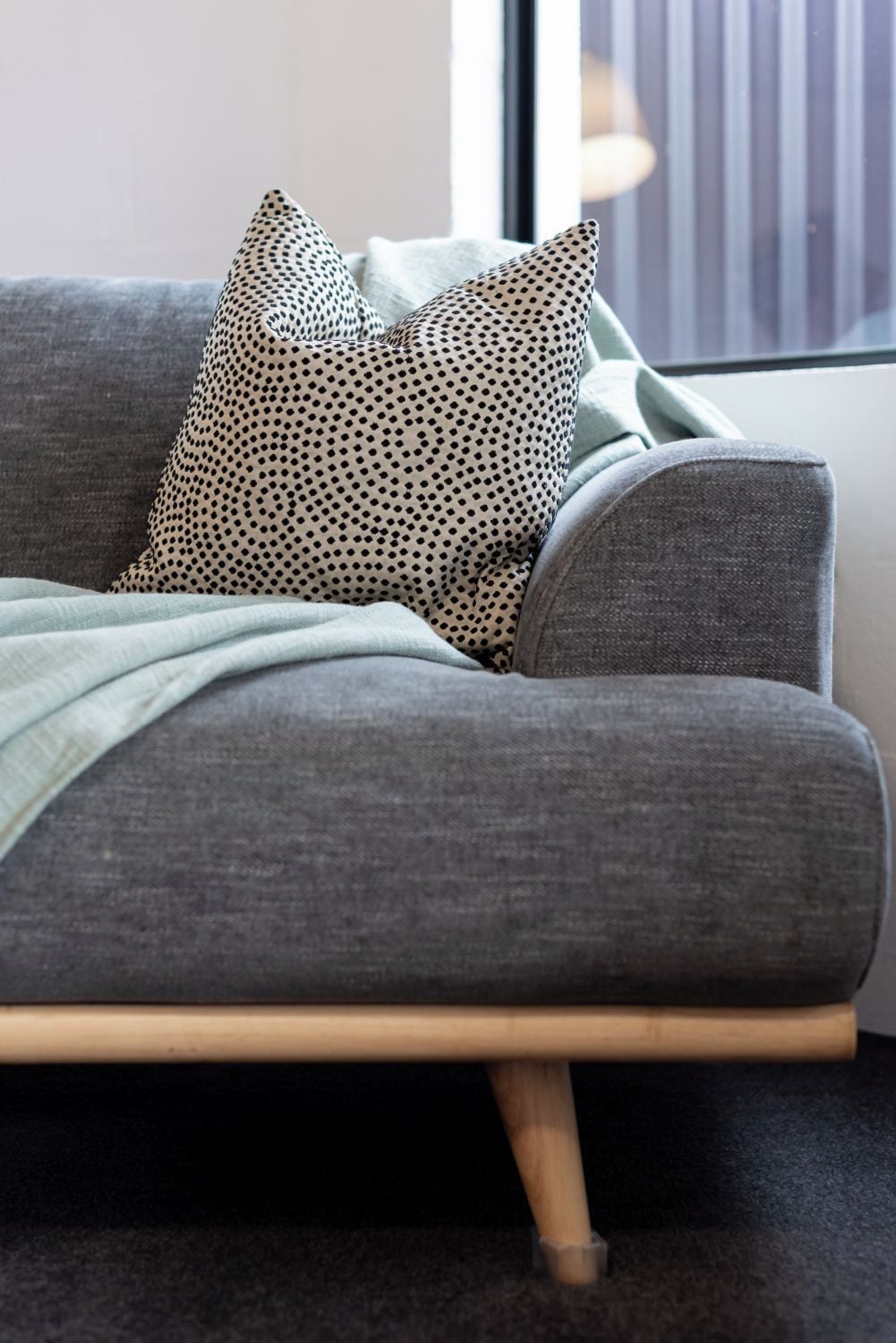 A grey sofa with wooden legs and two patterned pillows.