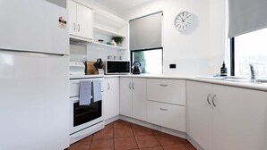Una cocina moderna con armarios blancos, horno empotrado, microondas y un reloj en la pared.
