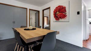 Un comedor moderno con una mesa de madera, sillas negras y un cuadro grande de una flor roja en la pared.