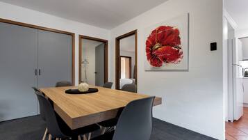 A modern dining area with a wooden table, black chairs, and a large red flower painting on the wall.