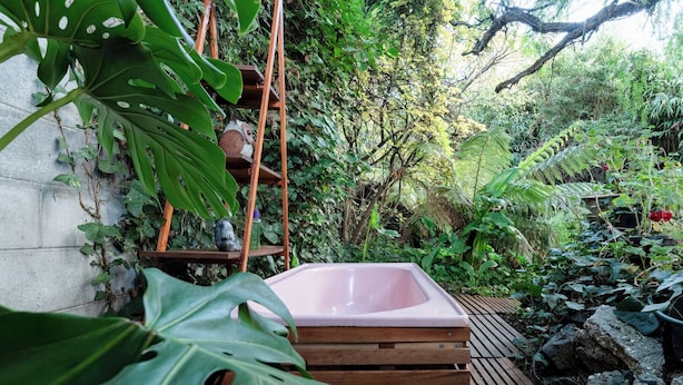A hot tub surrounded by lush greenery, wooden steps, and a concrete wall.