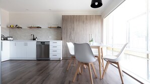 A modern kitchen with white cabinets, a built-in dishwasher, and a dining area with two white chairs and a table. - Cosy & Sweet: Near the City, WiFi & Parking (Launceston City)