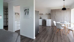 A modern kitchen with white cabinets, a dining area with a round table and chairs, and a hallway leading to a bedroom. - Cosy & Sweet: Near the City, WiFi & Parking (Launceston City)