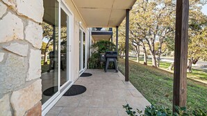 A covered patio with stone walls, a grill, and a view of a park.