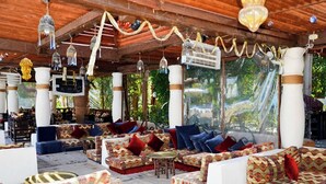 An outdoor seating area with patterned sofas and tables, surrounded by wooden pillars and hanging decorations. - Delta Sharm Apartments (Sharm El Sheikh)