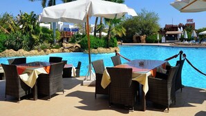 A poolside area with wicker furniture and umbrellas, surrounded by palm trees and a clear blue sky. - Delta Sharm Apartments (Sharm El Sheikh)