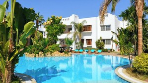 A pool area with a clear blue pool, lounge chairs, and a white building with balconies. - Delta Sharm Apartments (Sharm El Sheikh)