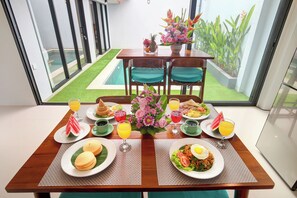 Ein Esstisch mit Frühstücksartikeln, einer Blumenarragemment und Blick auf Pool und Garten.