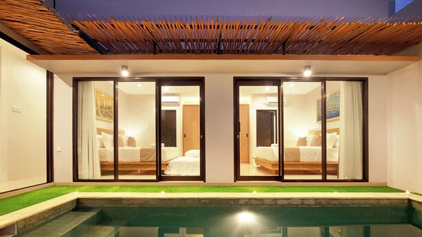 A modern hotel room with a glass door leading to a balcony, a private pool, and a well-lit interior.