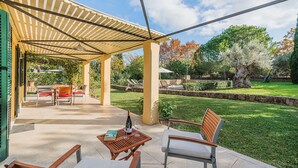 An outdoor patio with a pergola, a table with chairs, and a lawn area with trees and a stone wall. - Villa La Sort 140 - By Dream Villas Pollensa (Pollensa)
