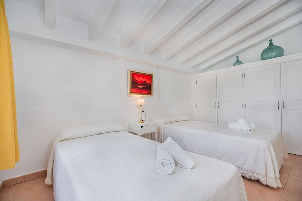 A hotel room with two beds, a painting on the wall, and a cabinet with vases.
