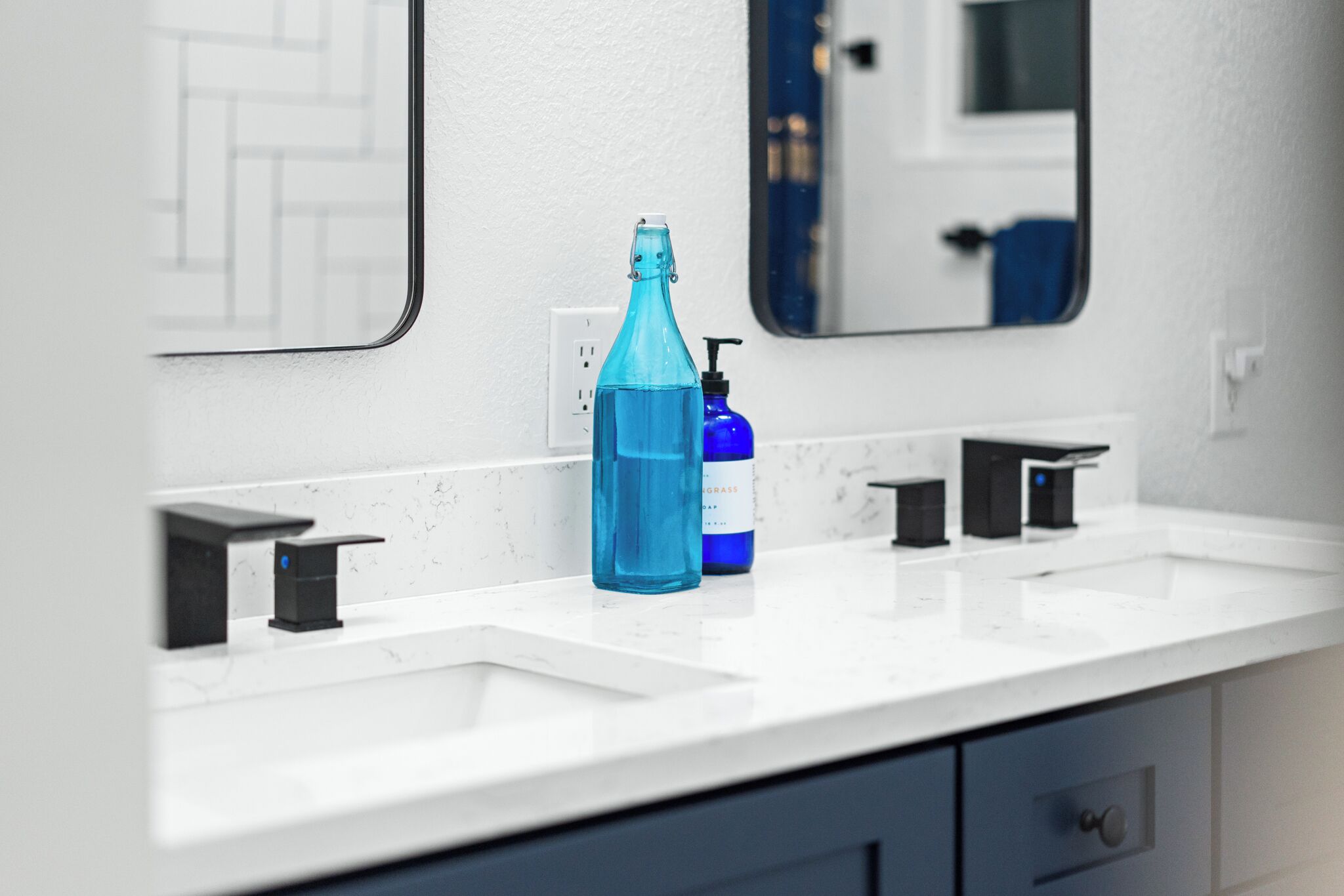 A bathroom with a white countertop, a blue bottle, and a blue soap dispenser.