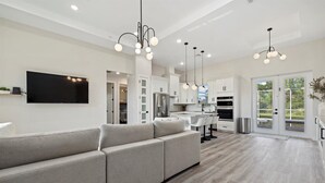 A modern kitchen with white cabinets, a built-in oven, and a dining area with a grey sofa and pendant lights. - Tropical Paradise in North Port! (North Port)