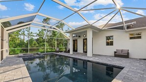 A modern outdoor pool area with a glass enclosure, stone flooring, and outdoor furniture. - Tropical Paradise in North Port! (North Port)