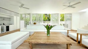A modern living room with a wooden coffee table, white sofas, and a kitchen area with white cabinetry. - Sunset Bungalow (Canggu)