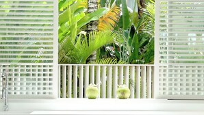 A white bathtub with a showerhead, surrounded by lush tropical plants and a white fence. - Sunset Bungalow (Canggu)