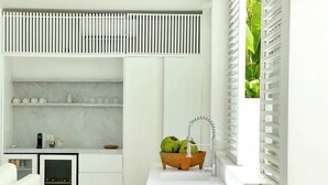 A modern kitchen with white cabinetry, a marble countertop, and a wooden bowl with fruits. - Sunset Bungalow (Canggu)
