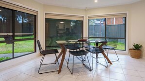 A dining area with a table and chairs, large windows, and a potted plant. - Relaxing 3bd in tranquil setting (Kennington)