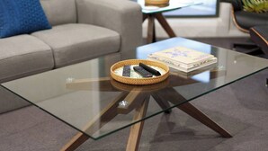 A glass-top coffee table with a woven basket containing remote controls, a book, and a small tray. - Relaxing 3bd in tranquil setting (Kennington)