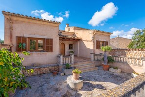 A traditional Mediterranean-style building with a stone facade, terracotta roof tiles, and a courtyard with potted plants.