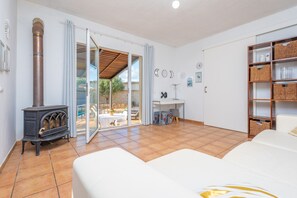 A spacious room with a large bed, a wooden stove, a dining area, and a view through a glass door.