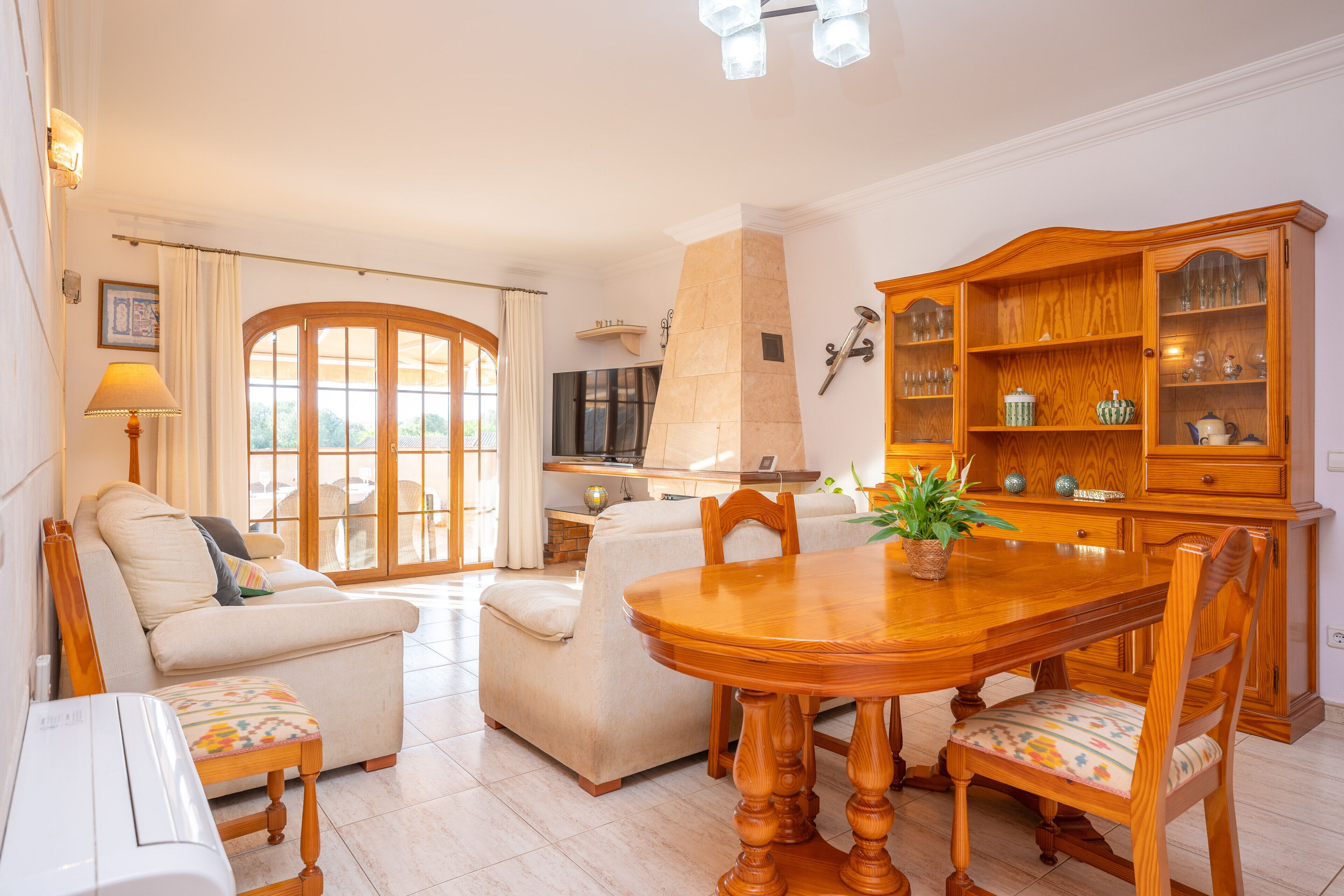 A living room with a wooden dining table, two sofas, a TV, and a cabinet with glassware.