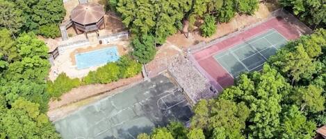 Vista aérea de una propiedad con piscina, canchas de tenis y un pabellón.