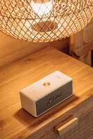 Un altavoz portátil sobre una superficie de madera con una lámpara tejida colgando arriba.