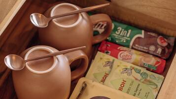 A wooden drawer containing a brown ceramic teapot, two spoons, and several coffee packets.