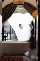 Ein modernes Badezimmer mit einer großen Badewanne, einer Duschkabine und einem Fenster mit Vorhängen.